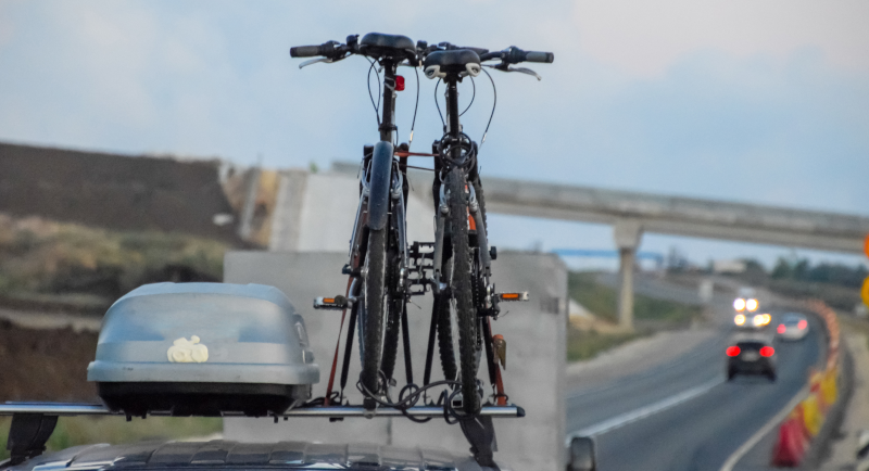 Zwei Fahrräder und eine Dachbox auf einem Auto, das auf der Autobahn fährt.
