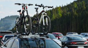 Zwei Fahrrädern auf einem Autodach, das neben vielen anderen auf einem Parkplatz steht.