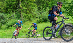 Drei Mountainbiker fahren auf ihren Rädern auf einem Schotterweg bergauf.