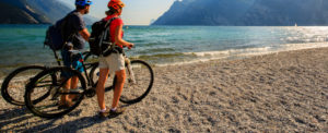Ein Paar mit Fahrradhelmen und Fahrrädern am Strand des Gardasees.