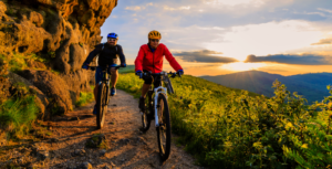 Ein Mann und eine Frau auf ihren Mountainbikes in einer bewaldeten Landschaft bei Sonnenuntergang.
