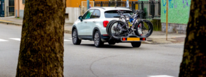 Ein weißes Auto in einer Straß, das ein Fahrrad am Heckträger transportiert.