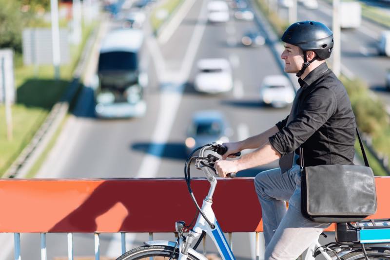 Junger Mann mit gebrauchtem E-Bike auf einer Brücke